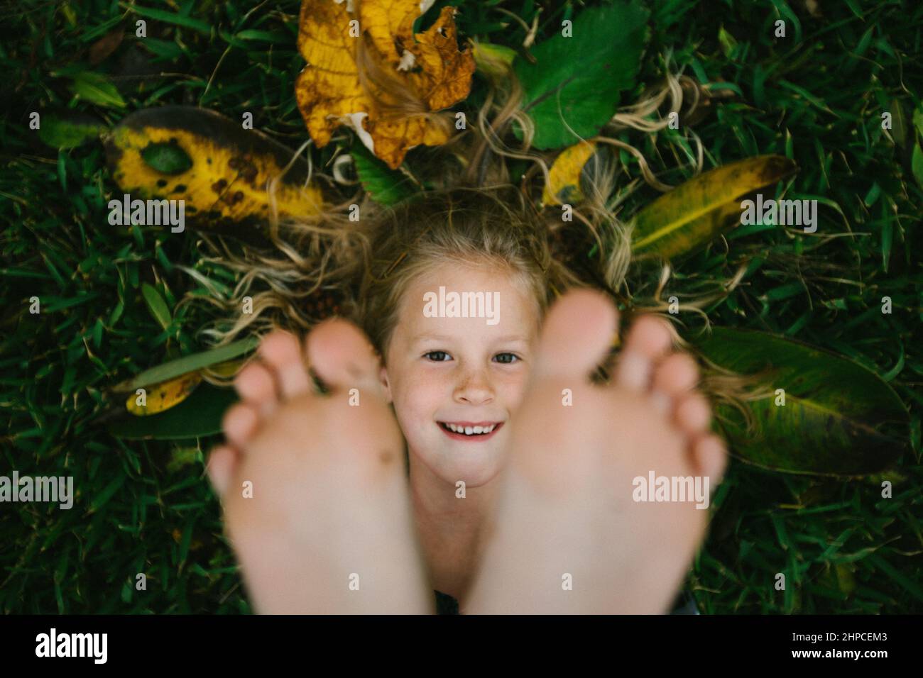 Playful girl smiling face framed by feet with grass and leaves Stock Photo