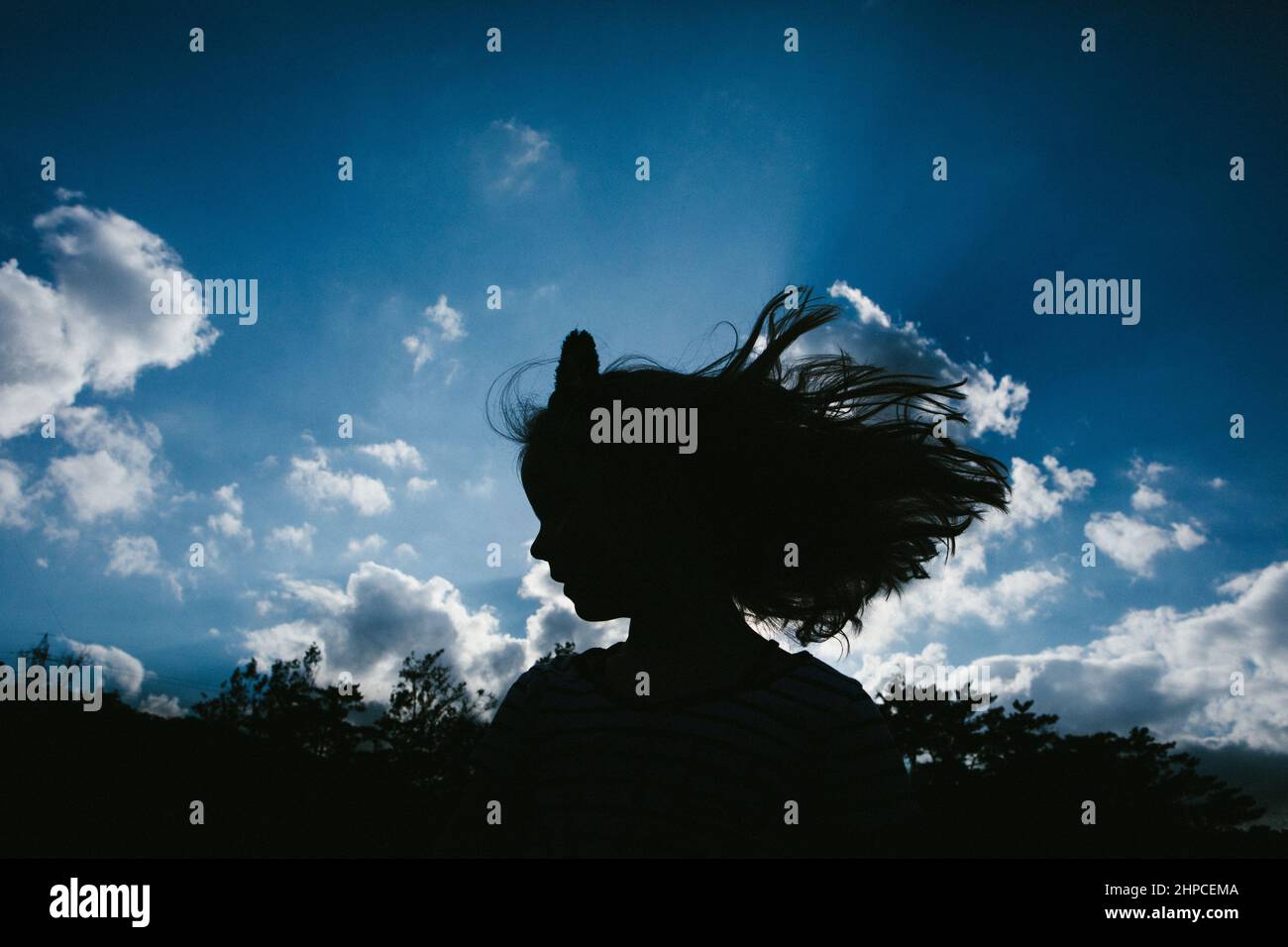 Long hair girl silhouette in front of sunny blue clouds sky Stock Photo
