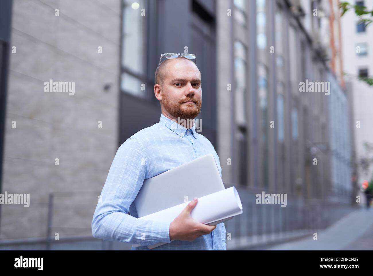 Portrait a successful and confident businessman. Young smiling stylish bearded business man standing on a street. Urban background of a modern office building in downtown. High quality image Stock Photo