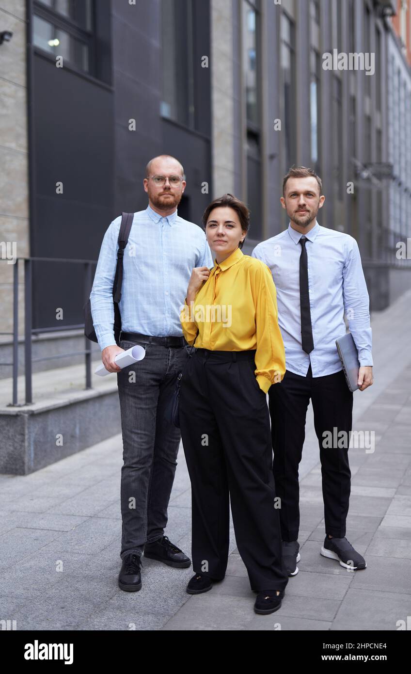Handsome confident caucasian woman in yellow blouse and two men looking at camera smiling. Medium shot portrait of successful professional business team posing outdoor in downtown. High quality photo Stock Photo