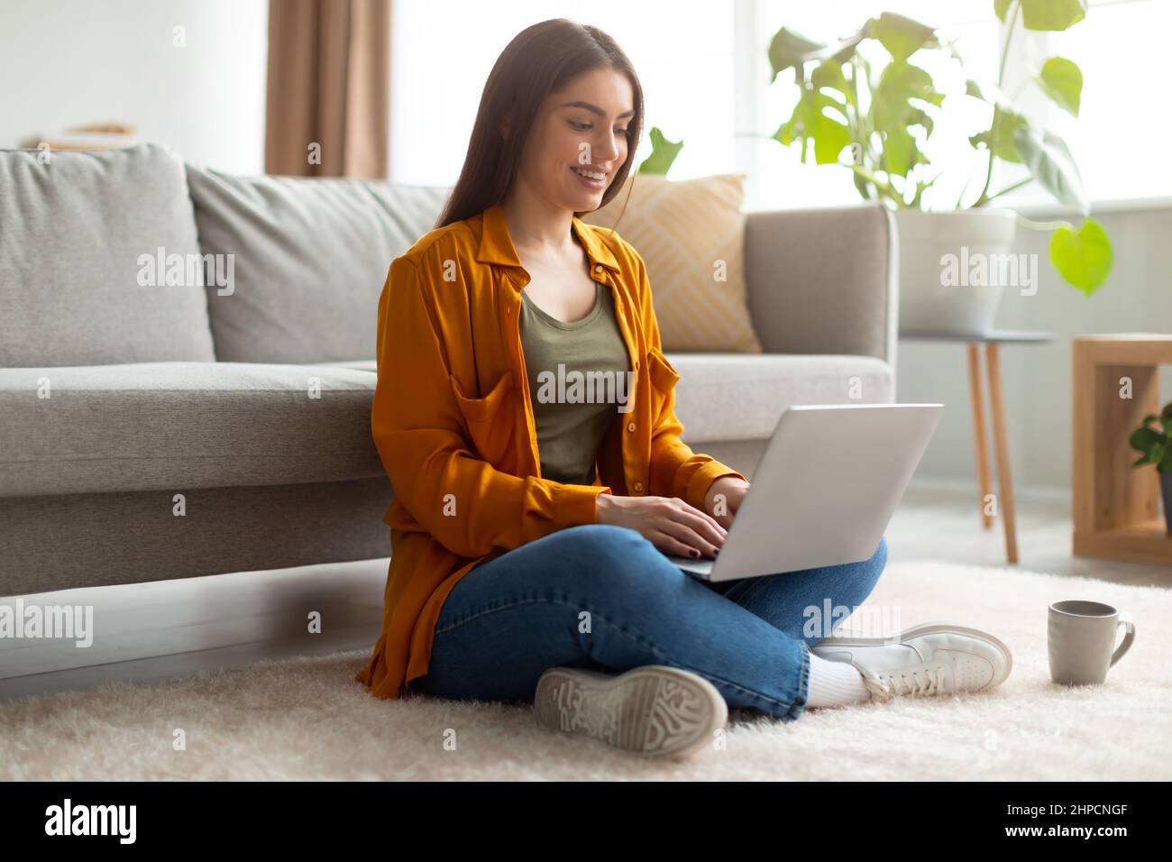Full length of happy young woman sitting cross legged on floor with ...