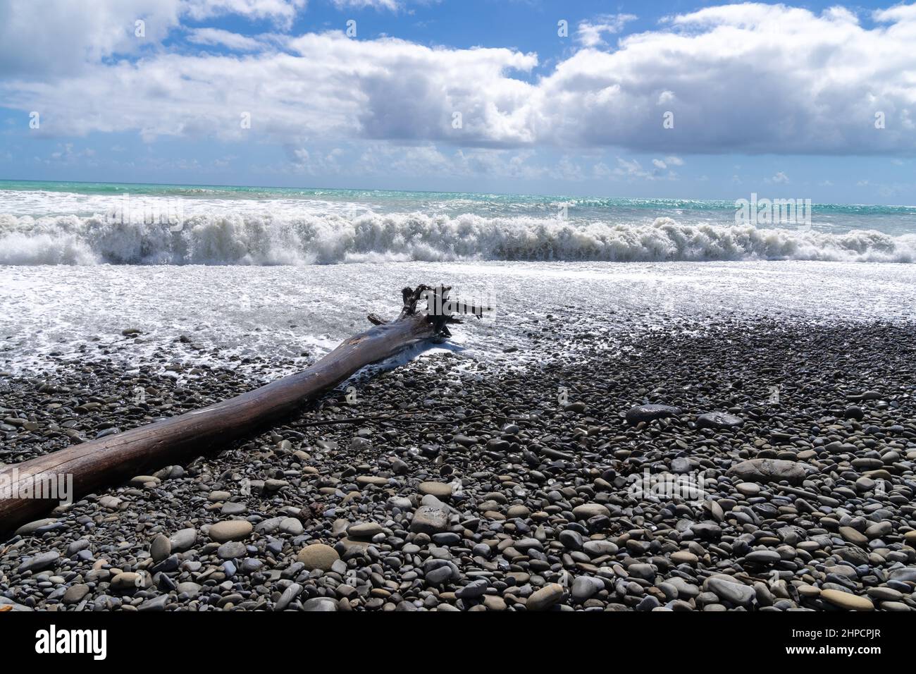 Huge seas crashing on stony beach at Te Araroa aound large log on beach, on New Zealand's East coast. Stock Photo