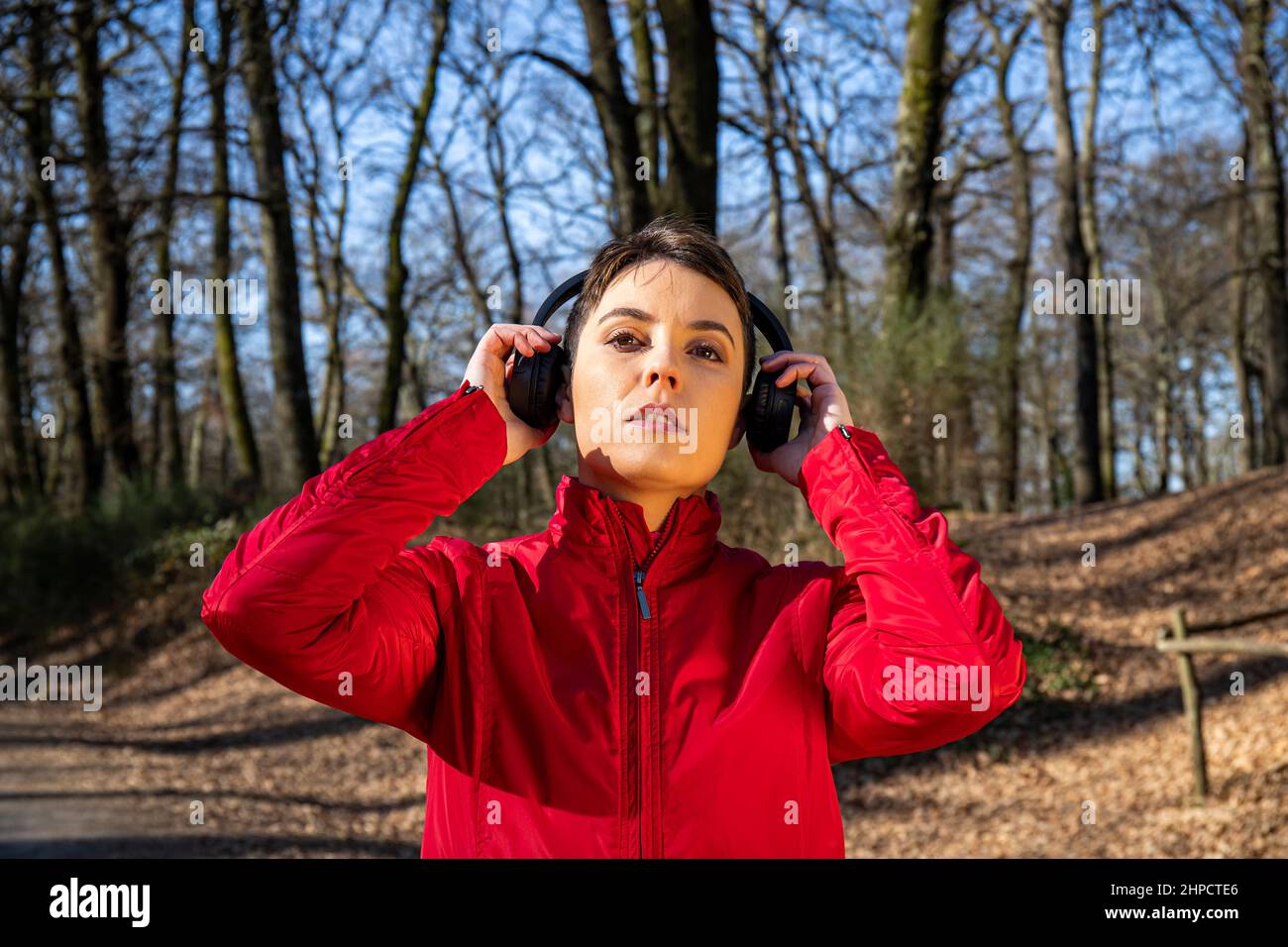 Young woman is training in the forest. Beautiful woman with short hair is listening to the music while she walks in the park. Stock Photo