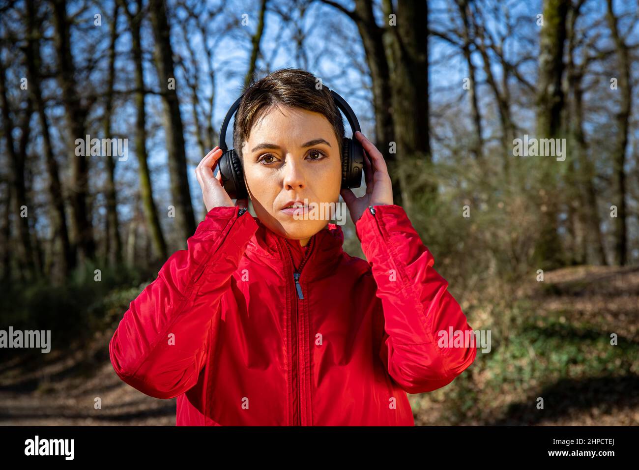 Young woman is training in the forest. Beautiful woman with short hair is listening to the music while she walks in the park. Stock Photo