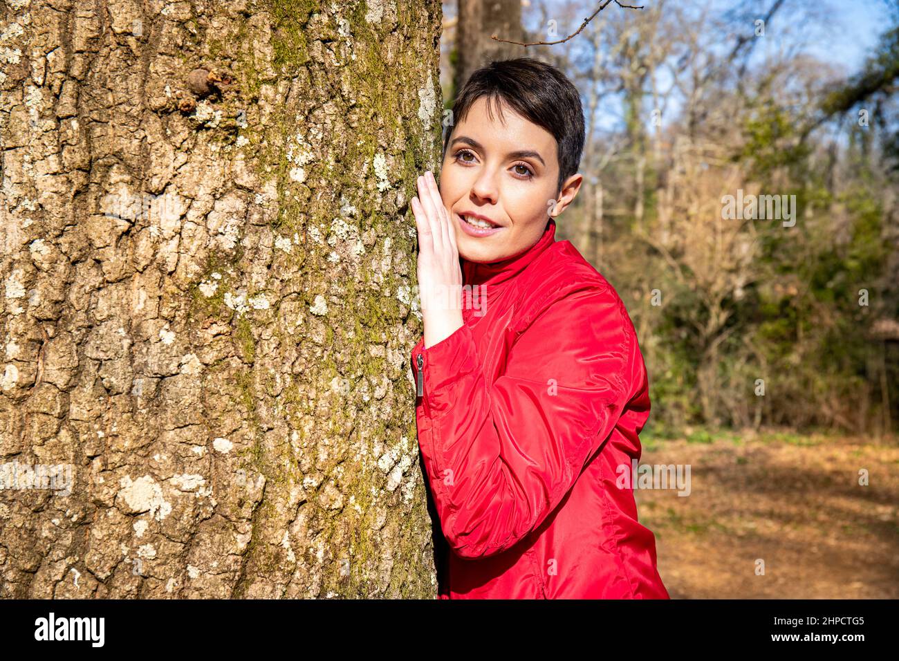 The young woman is hugging a large oak tree. The woman is touching the trunk and feeling the energy of nature. Concept of well-being and love for natu Stock Photo