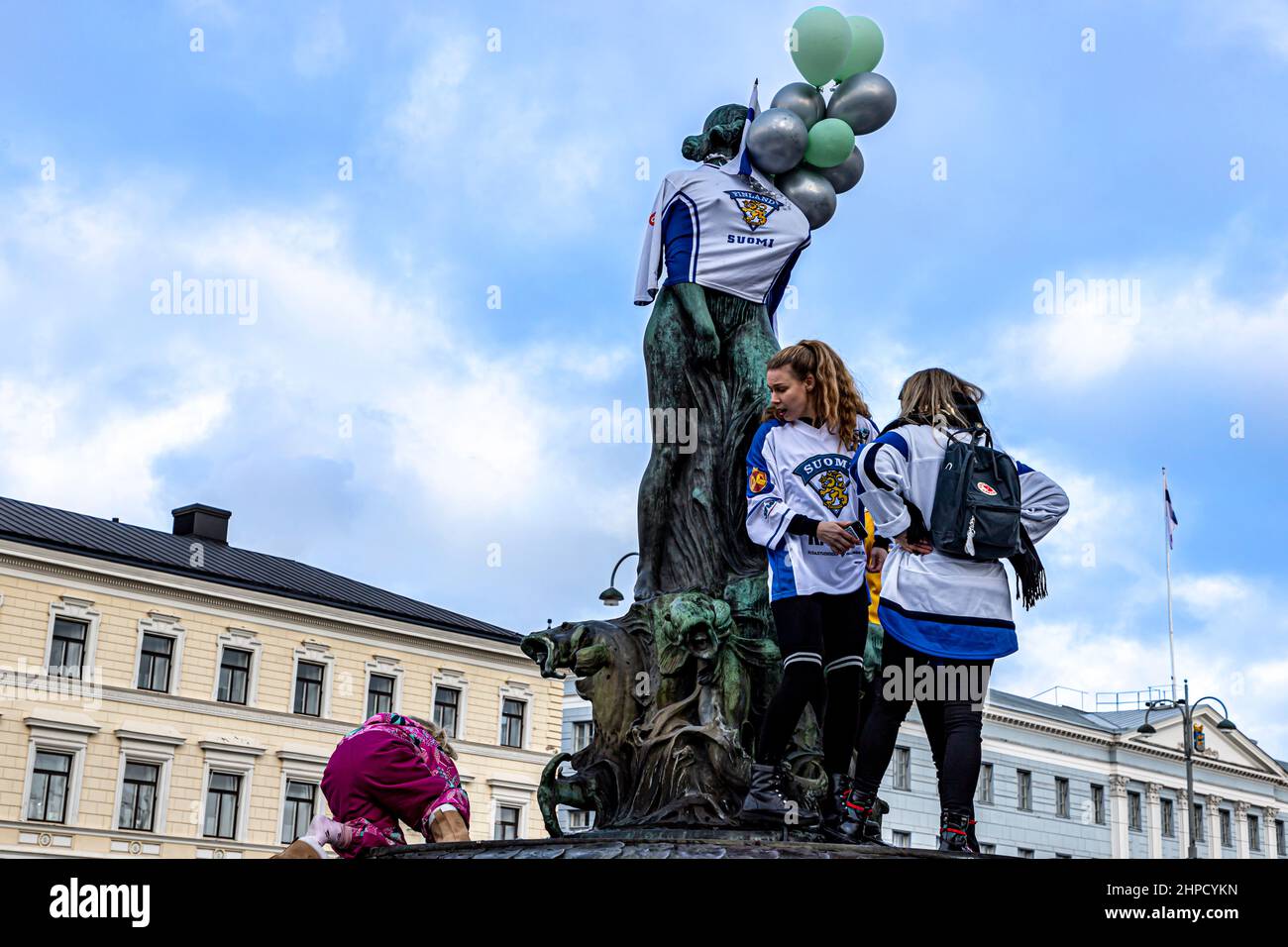 Hockey fans on the Havis Amanda statue in the Helsinki Market Square, one fan reacting to a small child being pushed up onto the statue. Stock Photo