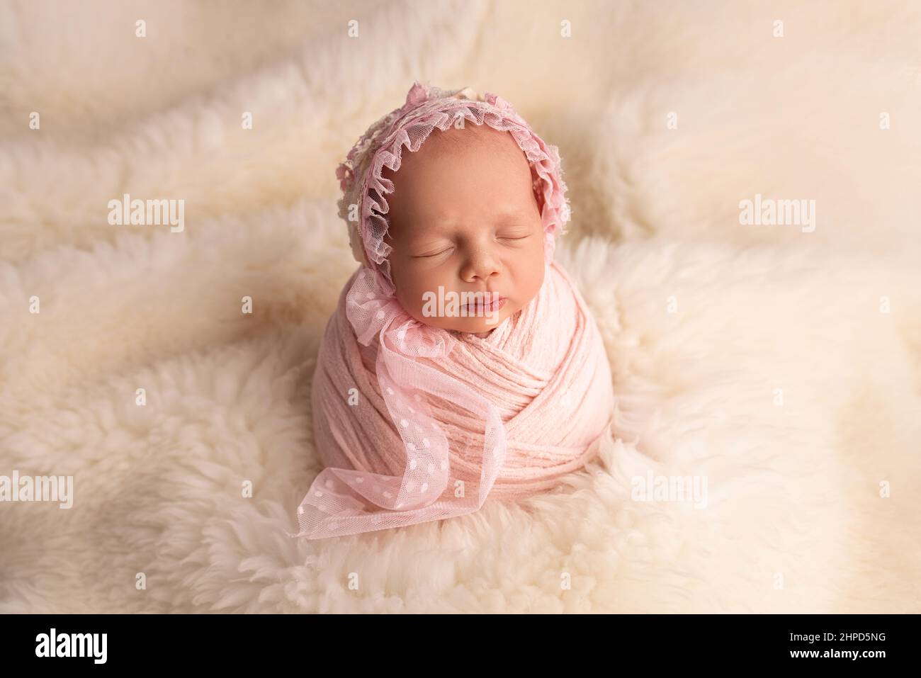Sleeping newborn girl in the first days of life in a pink cocoon with a pink cap on a white background. Stock Photo