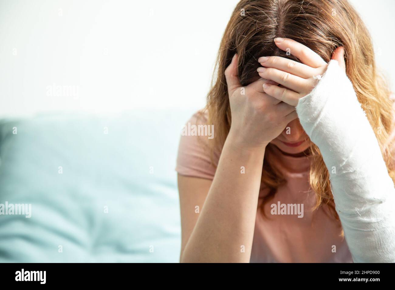 A woman with a plaster cast on her arm holds her head. Stock Photo