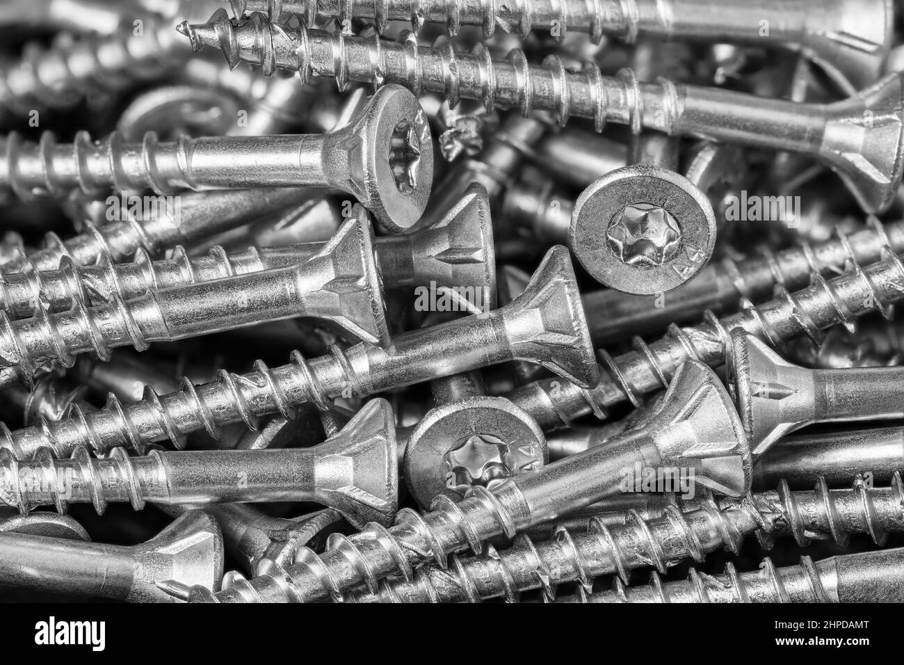 Stainless steel wood screws with thread and countersunk torx head in black and white texture. Close-up of metal fasteners heap in a tech background. Stock Photo