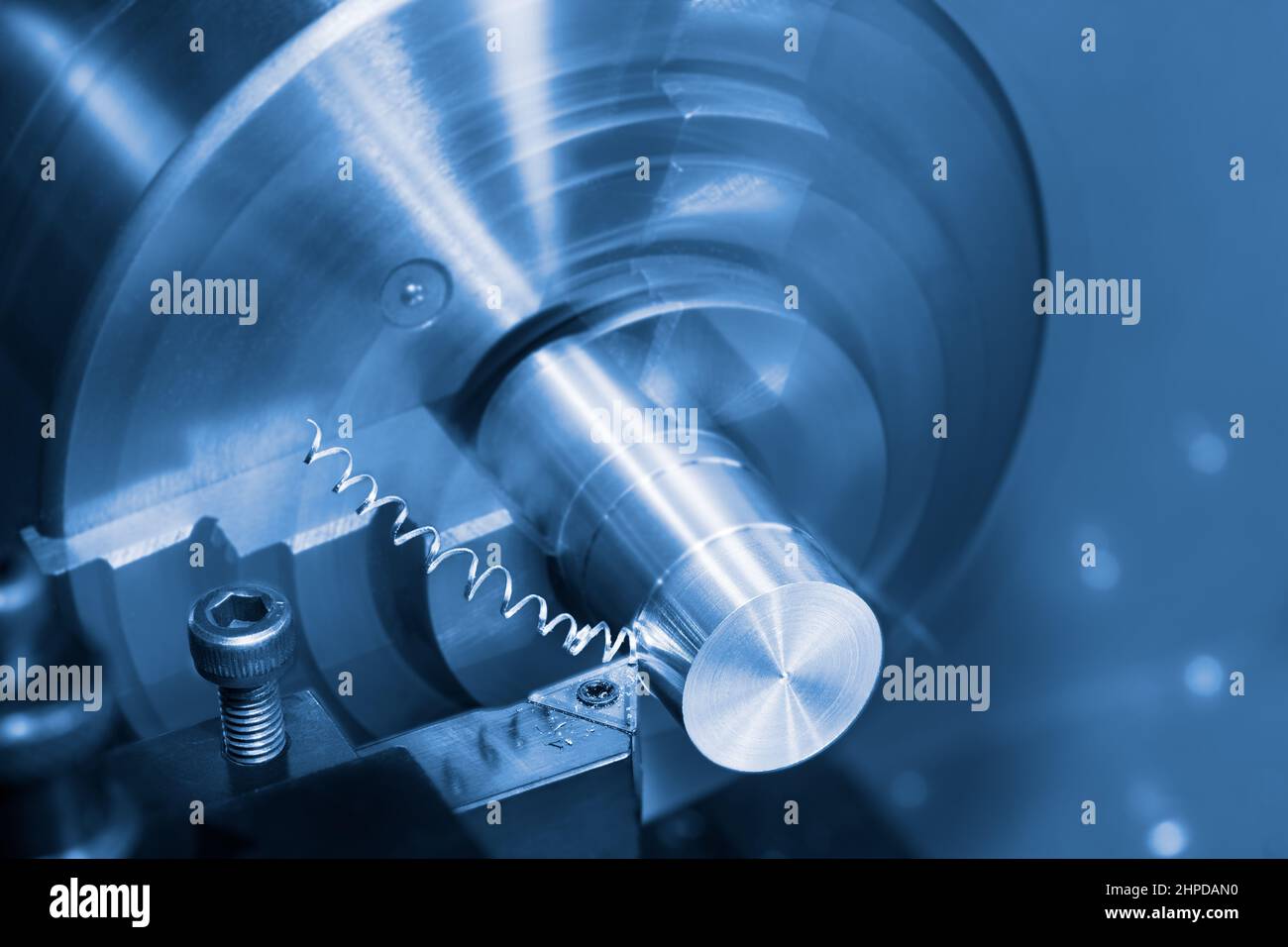 Lathe tool bit and spiral swarf at working on a metal product. Close-up of steel knife with carbide insert and turning machine. Blue toned background. Stock Photo