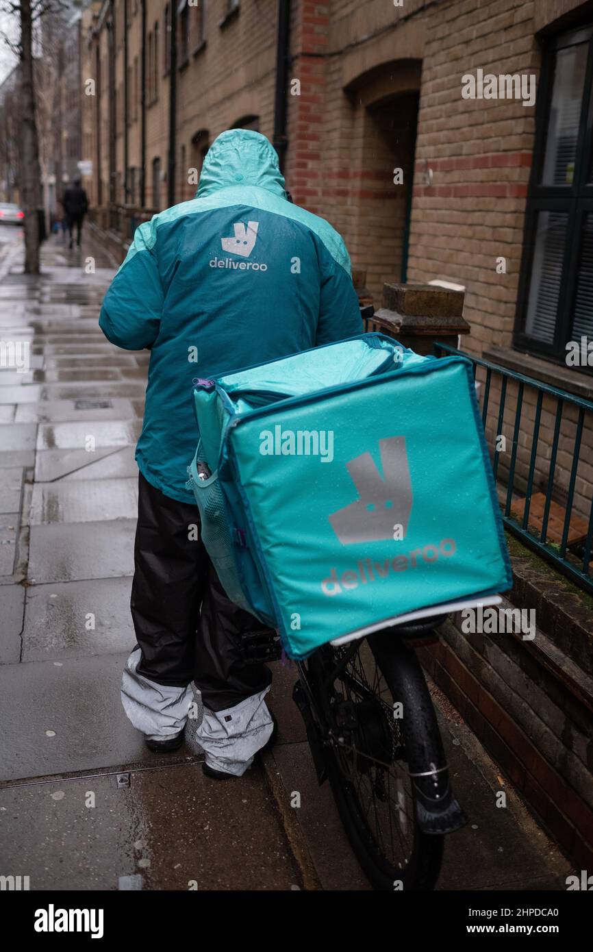 Deliveroo driver adjacent his bike on a wet winters day in London. Through an app anyone can order take away to be delivered to their home. Stock Photo
