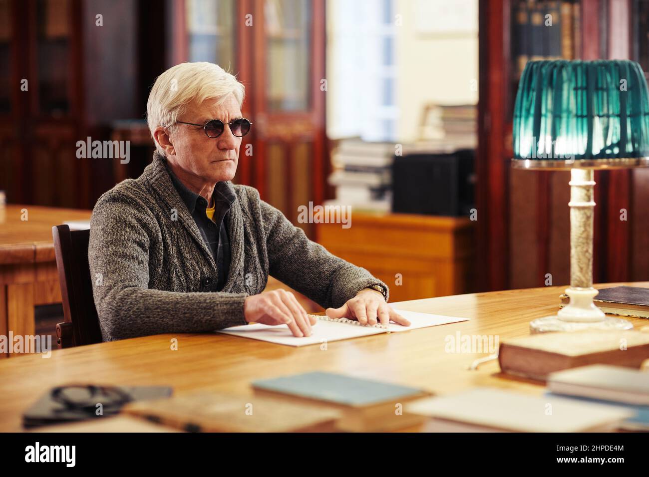 Portrait of senior man with vision impairment reading book in braille at table in classic library Stock Photo