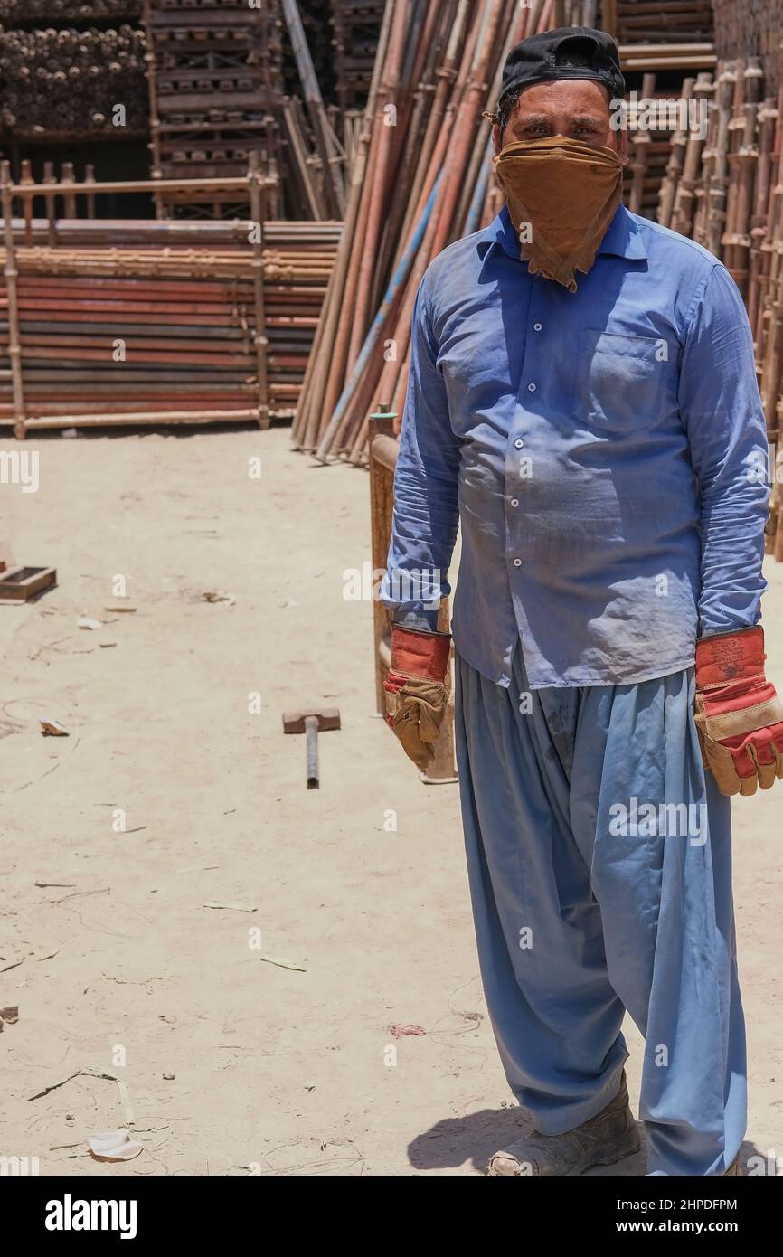 Mature middle eastern migrant laborer wearing muslim male headdress, working for scrap metal supply warehouse for recycling and posing for photo. Abu Stock Photo
