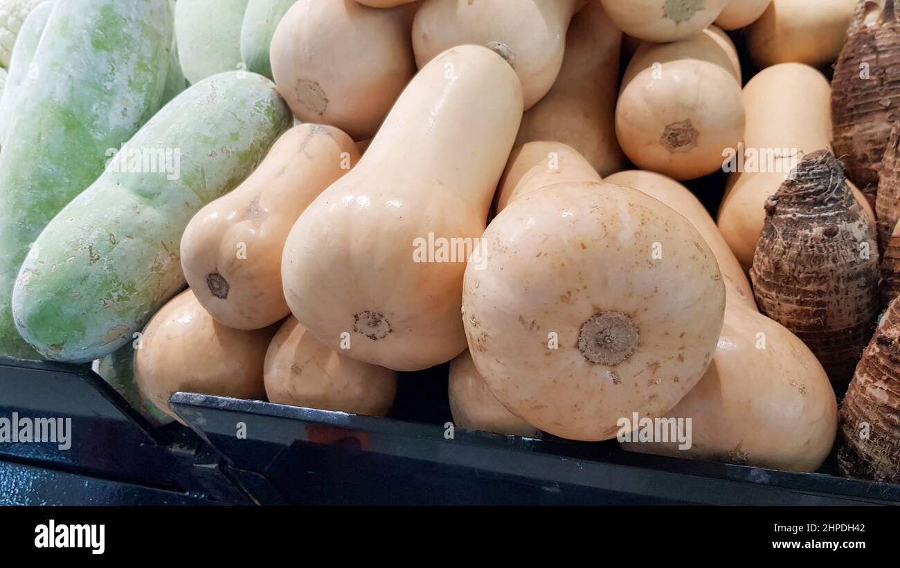 Butternut pumpkins are placed on shelves for sale along with other agricultural products. Stock Photo