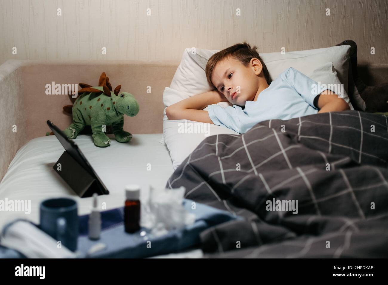 Very sad ill child laying in bed with toys and tablet Stock Photo