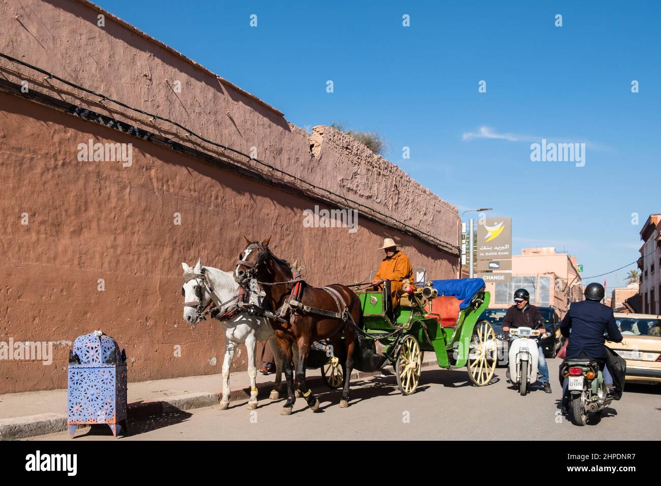 Moroccan people travel through the streets of Marrakech by horse drawn buggy, motorcycles, and cars. Stock Photo