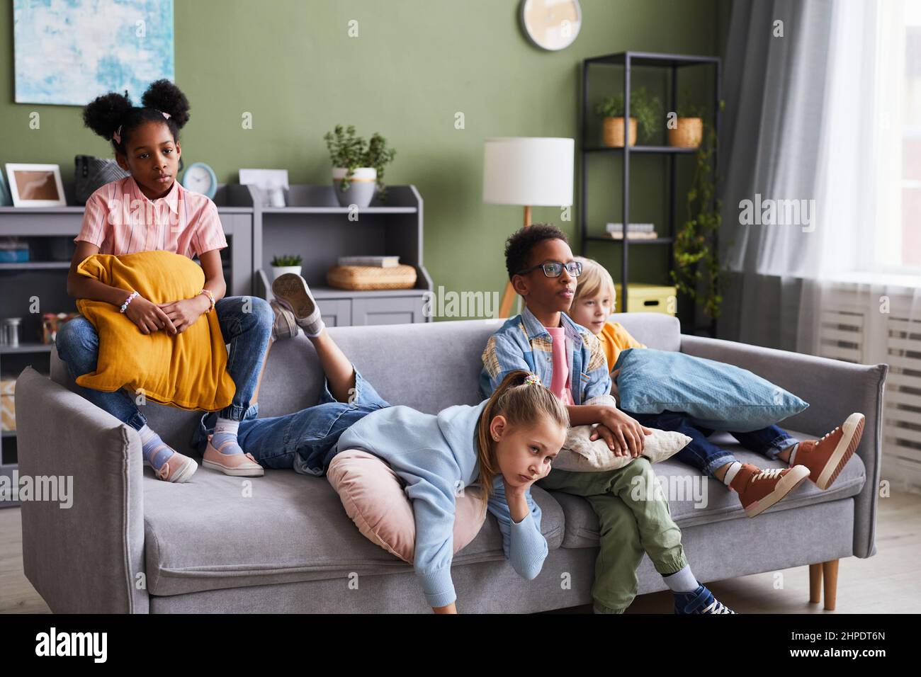 Diverse group of children watching TV at home while lounging on sofa looking bored Stock Photo