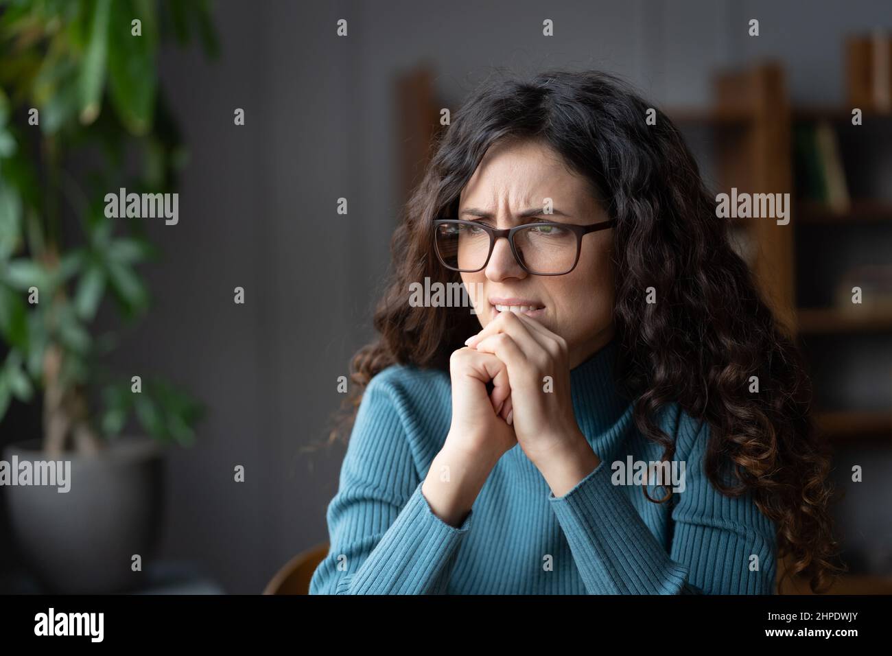 Young nervous stressed female plagued by constant worries and anxious thoughts while sitting at home Stock Photo