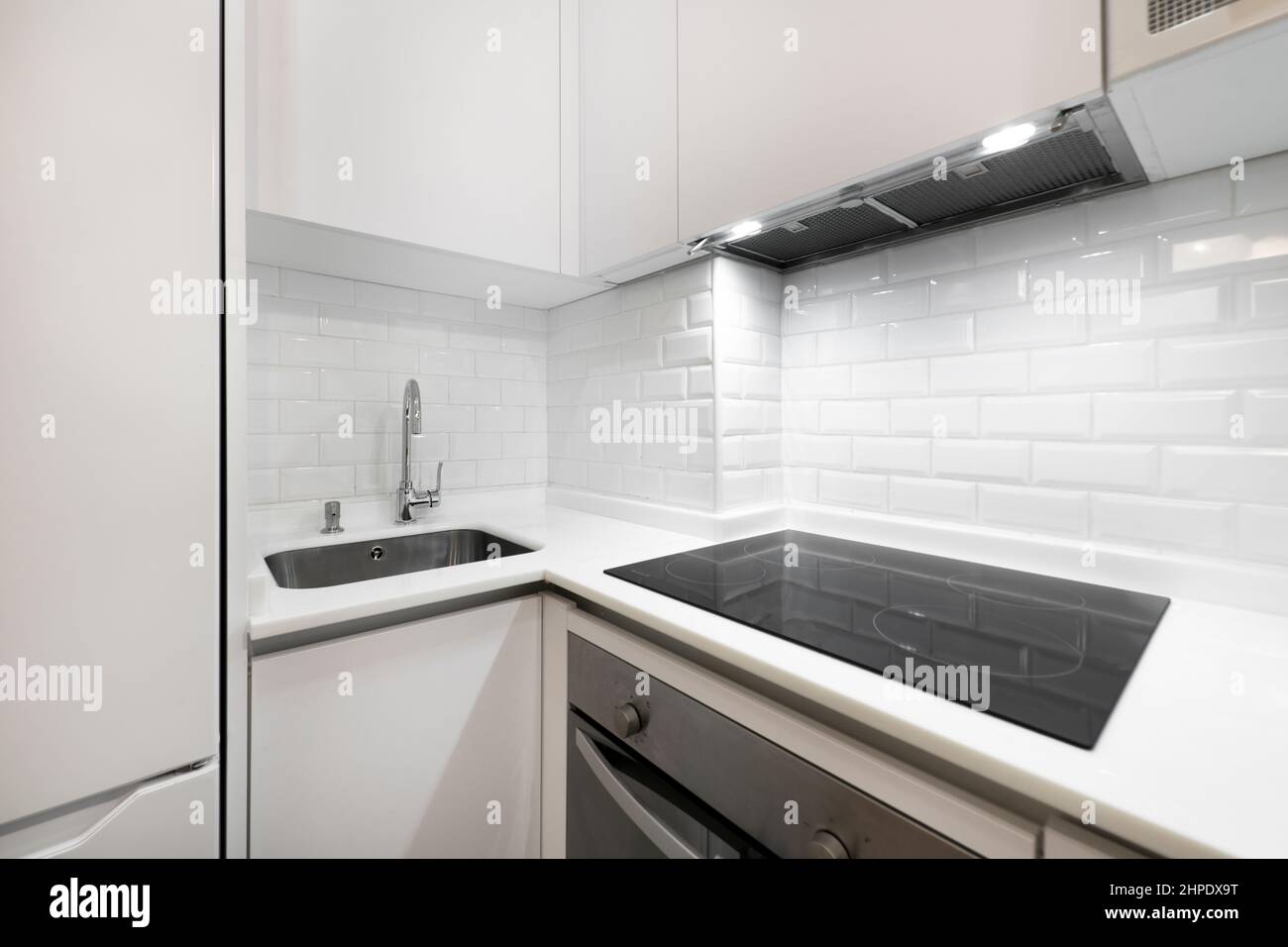 Corner of a modern kitchen with ceramic hob, extractor hood, stainless steel oven, sink embedded in the stone composite countertop Stock Photo