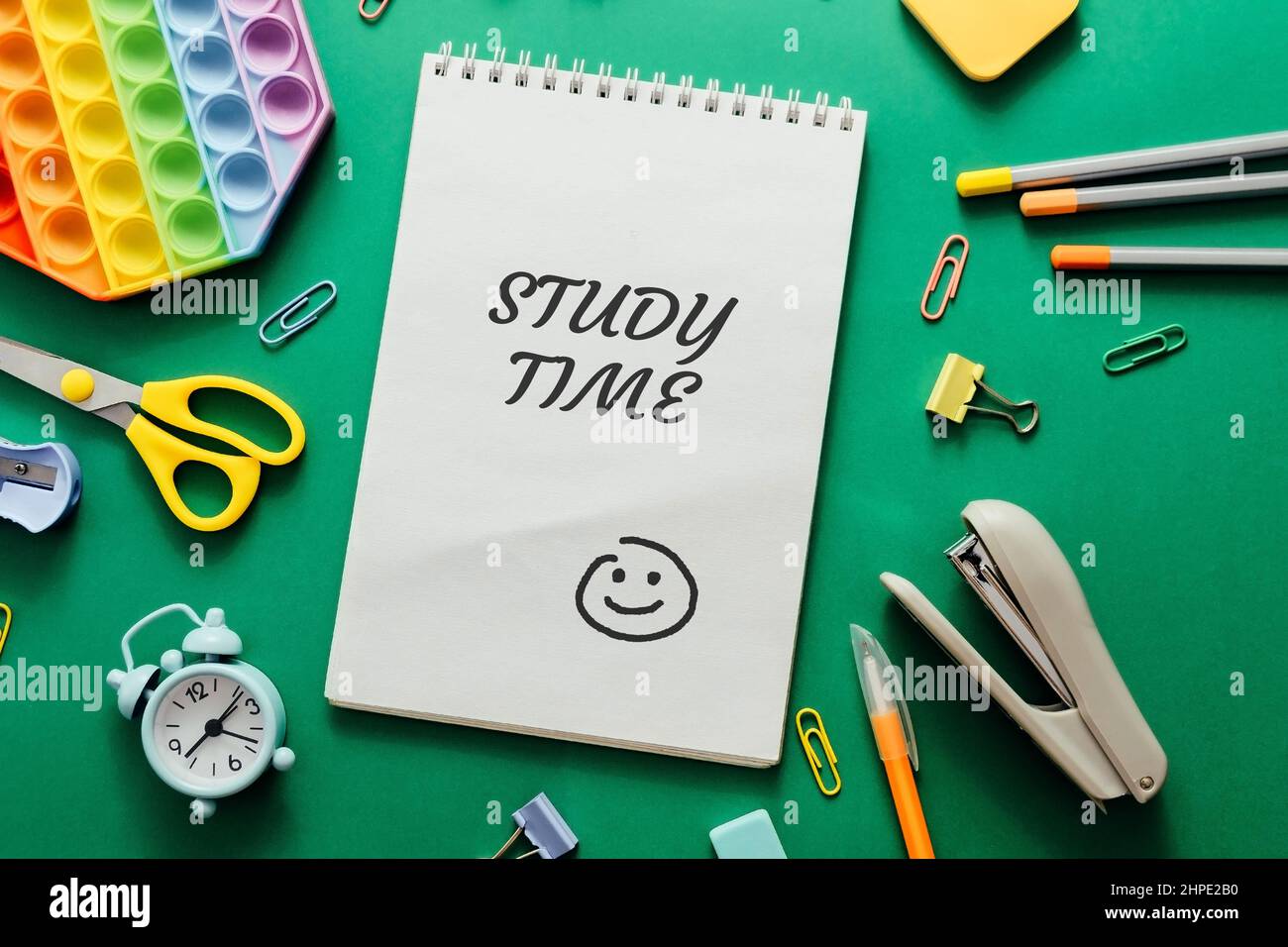 notebook on green background with text Study Time.Colored various school supplies and an alarm clock on a green paper background. Stock Photo
