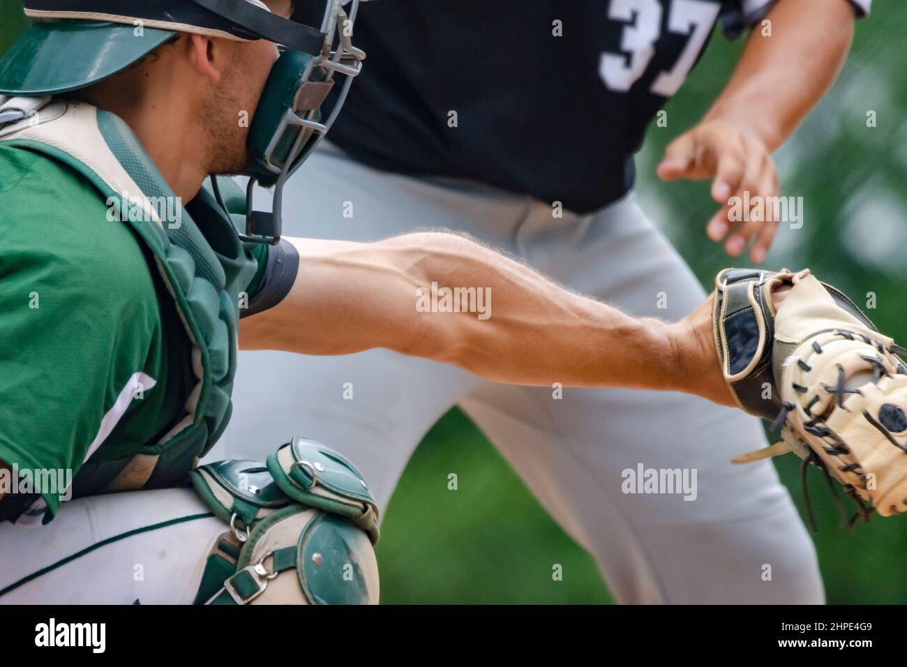 A catcher receives the pitch as the batter watches the ball.  Batter blurred in background. Stock Photo