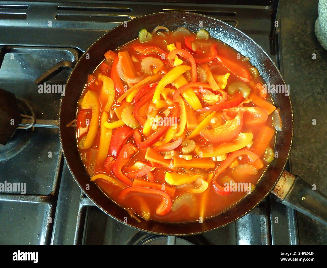 Red and yellow capsicum (bell peppers) form the basis of this summer vegetable dish, simmering in a large frypan on a gas hob Stock Photo