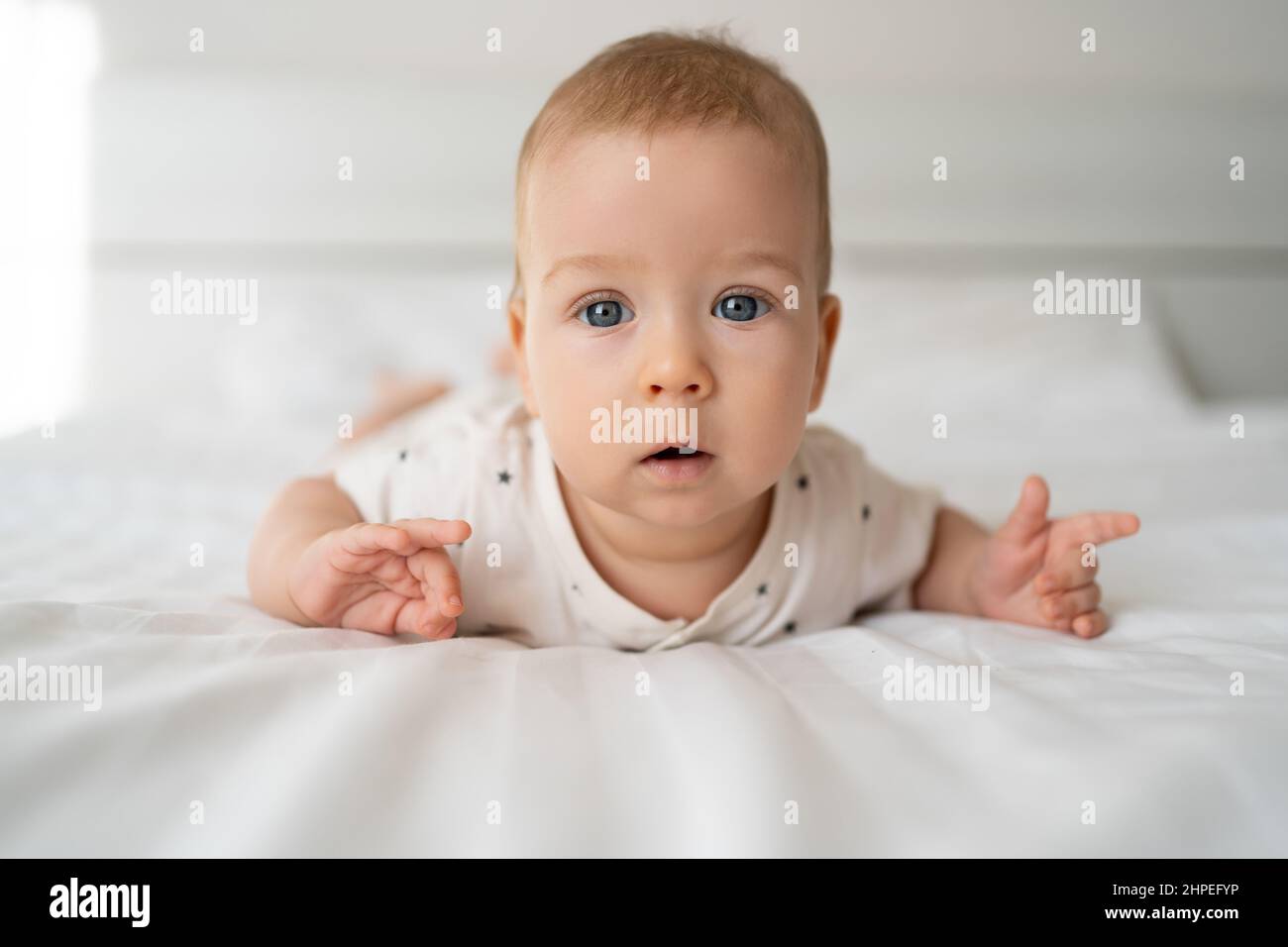 Portrait of a baby with blue eyes lying on a white bed, dressed in a