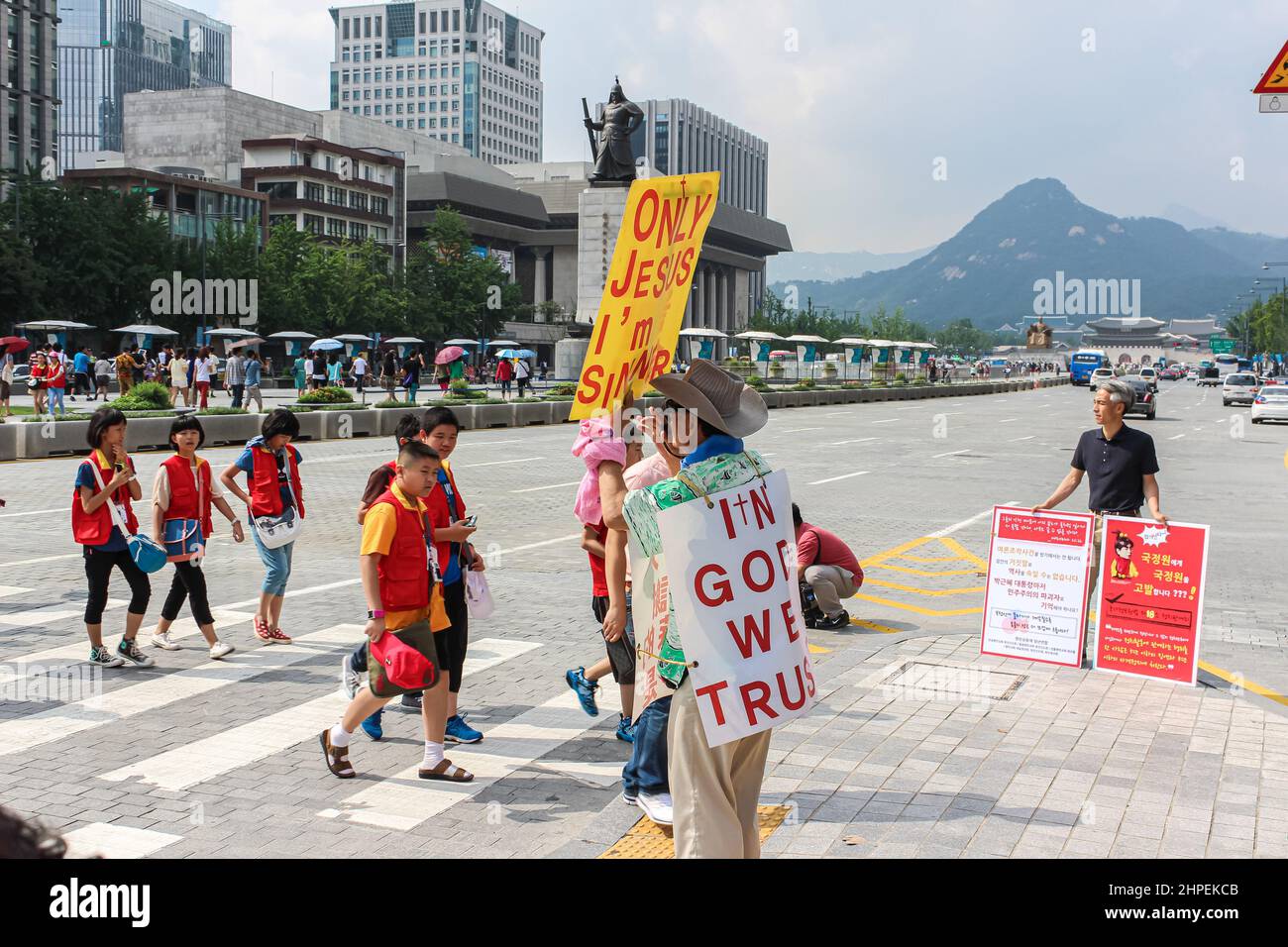 Seoul, South Korea - July 24th, 2020: Man praising Jesus on the main road of Seoul. In the background the Statue of Sejong the Great. Group of childre Stock Photo