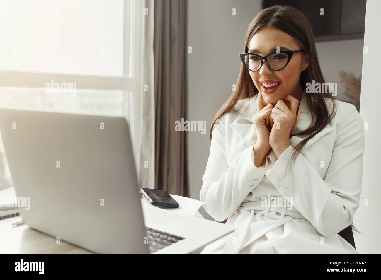 Beautiful happy young businesswoman, woman using laptop and smiling while working indoors. Home office during Coronavirus or Covid-19 quarantine. Comm Stock Photo