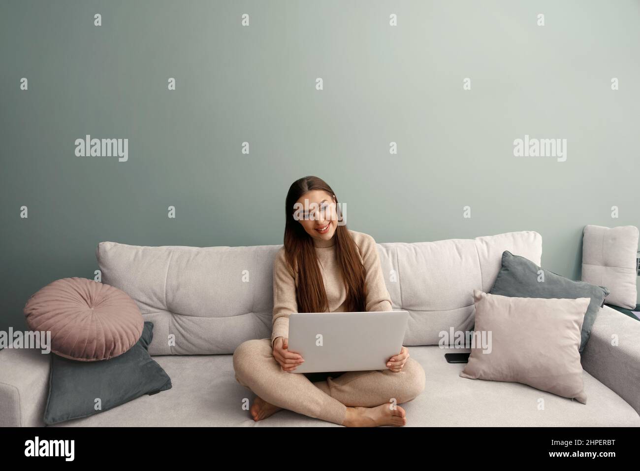 Smiling young woman using laptop, sitting on couch at home, beautiful girl shopping or chatting online in social network, having fun, watching movie, Stock Photo