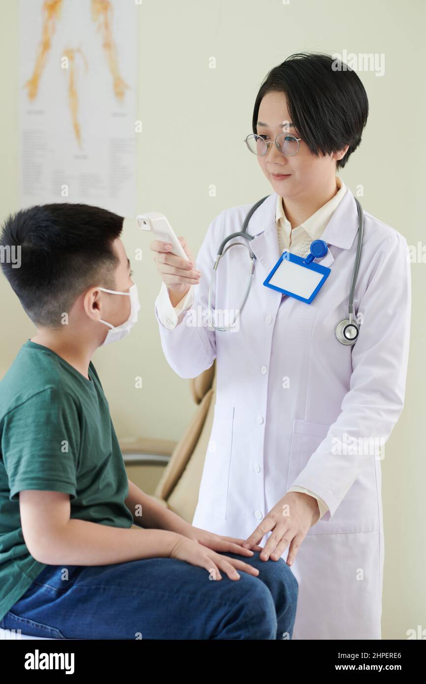 Asian female doctor in white coat checking the temperature of little