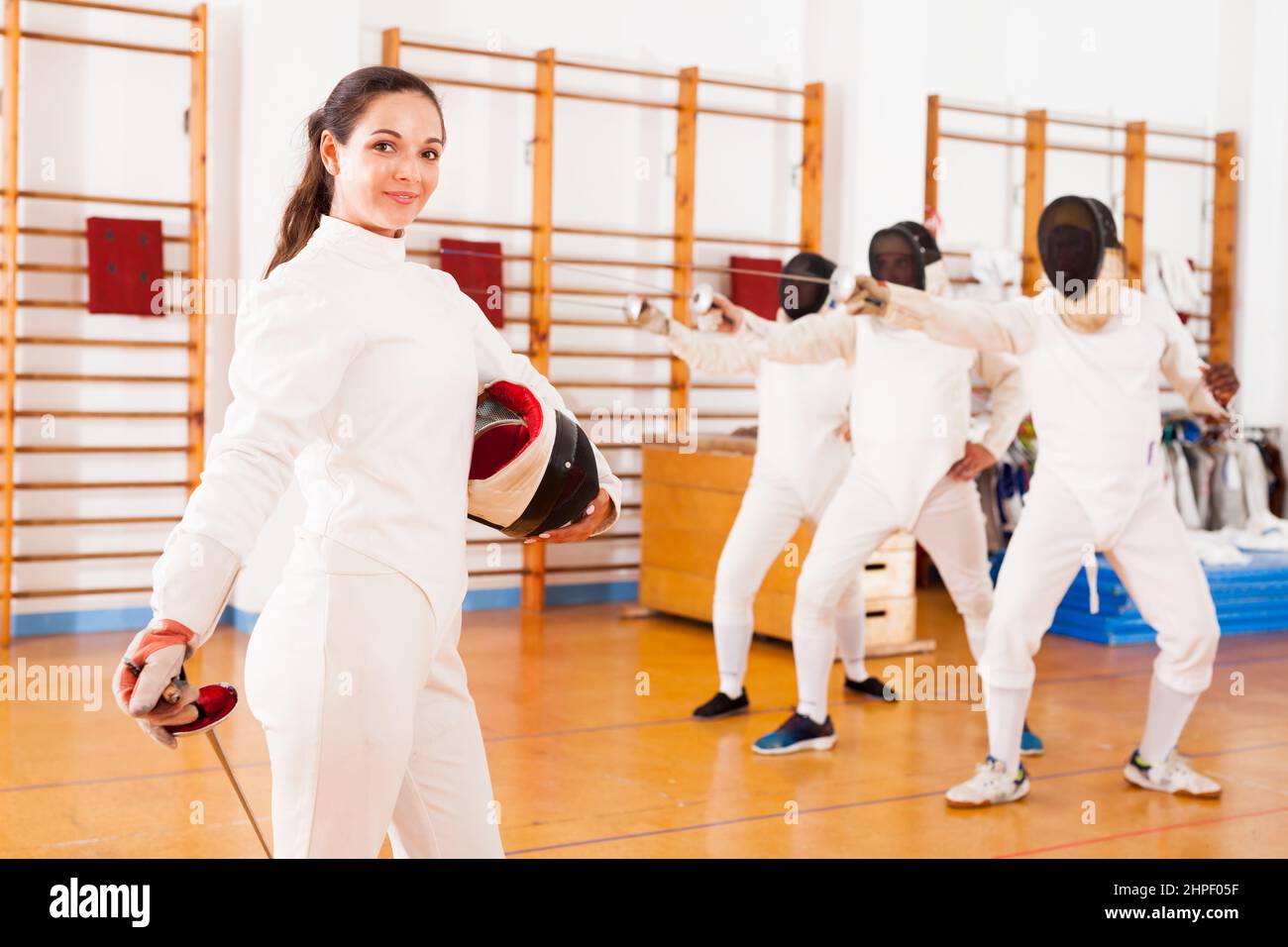 Positive active young female fencer standing at fencing workout Stock Photo