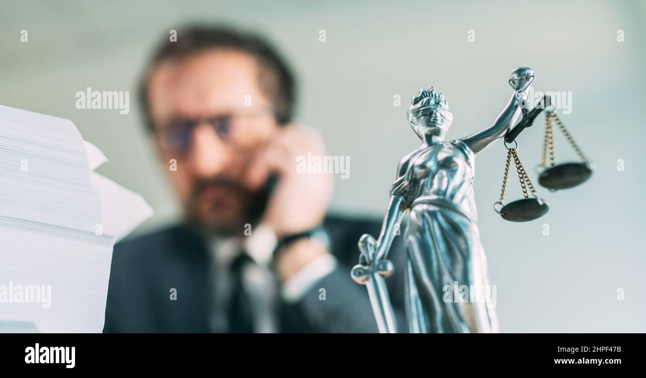 Lawyer on the phone, attorney talking on smartphone from his office with Lady Justice statue on desk, selective focus Stock Photo