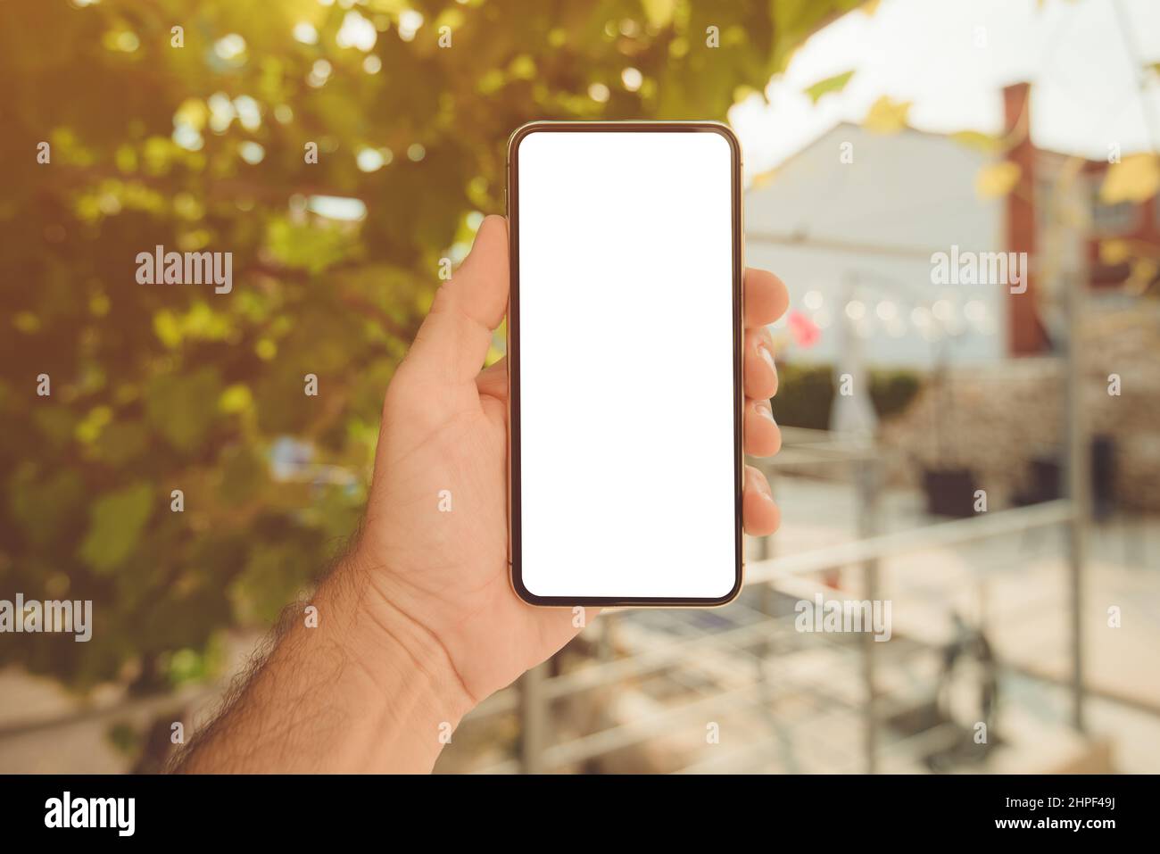 Man holding mobile smart phone with blank mock up screen in home backyard on sunny summer morning, close up with selective focus Stock Photo