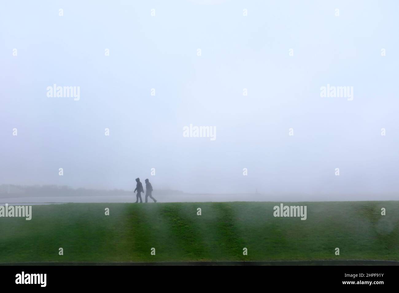 09.02.2022, Cuxhaven, Niedersachsen, Deutschland - zwei Spaziergaenger im Regen auf dem Deich an der Grimmershörner Bucht in Cuxhaven an einem Wintert Stock Photo