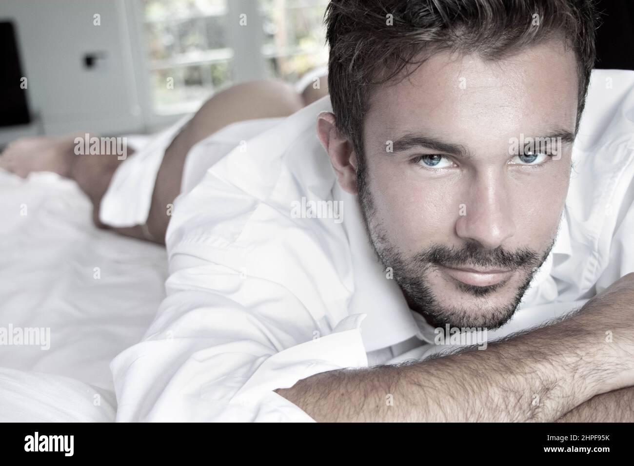 Portrait of handsome man with blue eyes and beard looking at camera with blurred naked behind in background Stock Photo