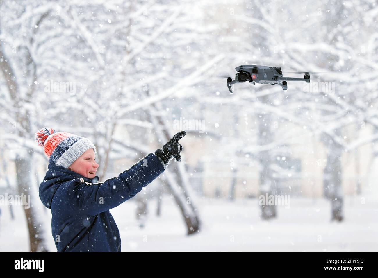 Teenager boy dressed winter jacket and modern digital drone DJI Mavic, flying in snow conditions. DJI Mavic 3 most portable drones with Hasselblad cam Stock Photo
