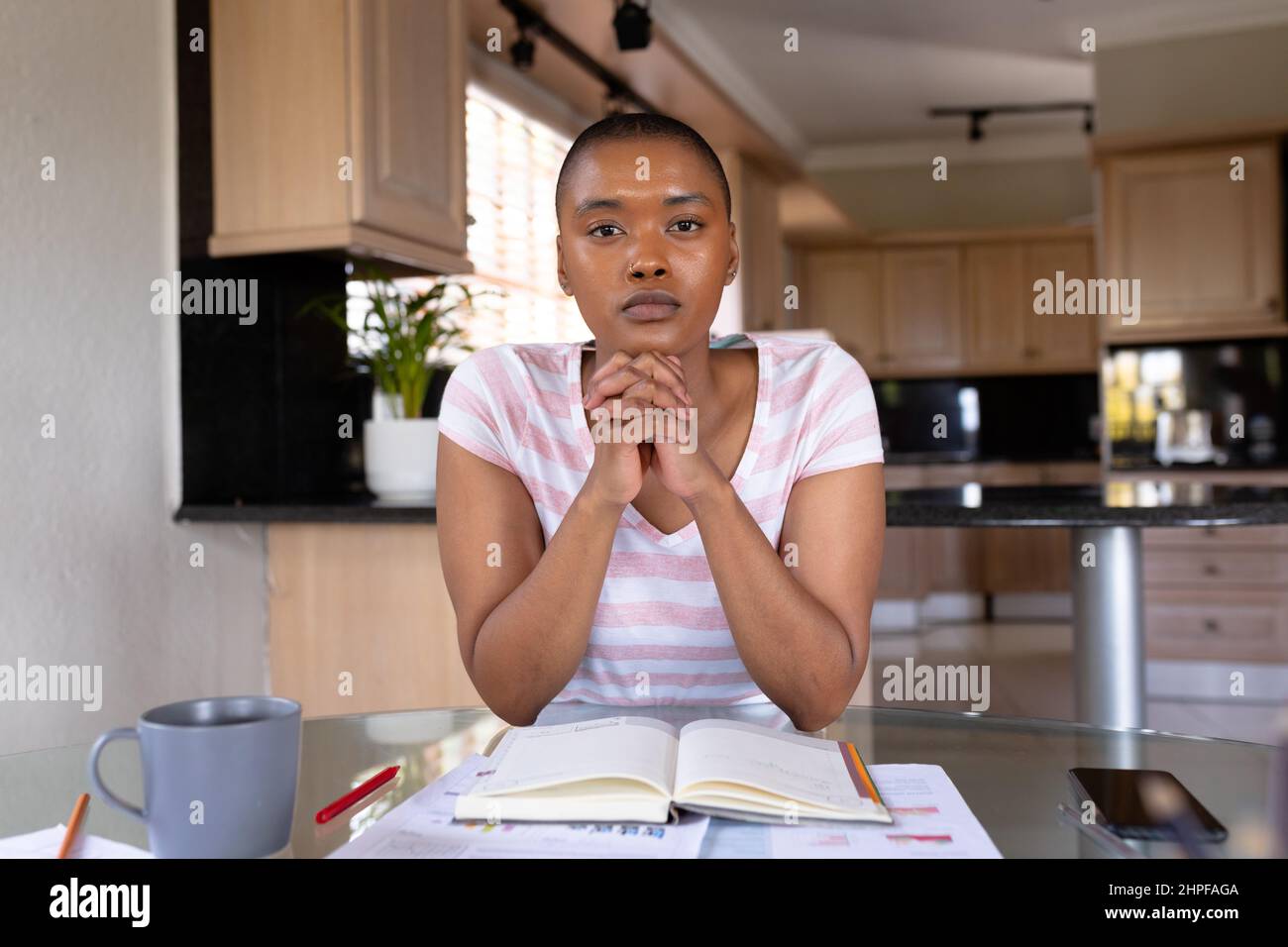 Portrait of biracial female freelancer sitting with hands clasped at home office Stock Photo