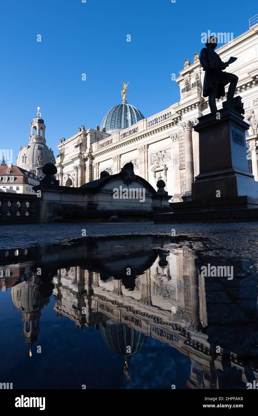 Dresden, Germany. 21st Feb, 2022. The Frauenkirche (l) is reflected in a puddle next to the Lipsius Building and the Gottfried Semper Monument on the Brühl Terrace. Credit: Sebastian Kahnert/dpa-Zentralbild/dpa/Alamy Live News Stock Photo