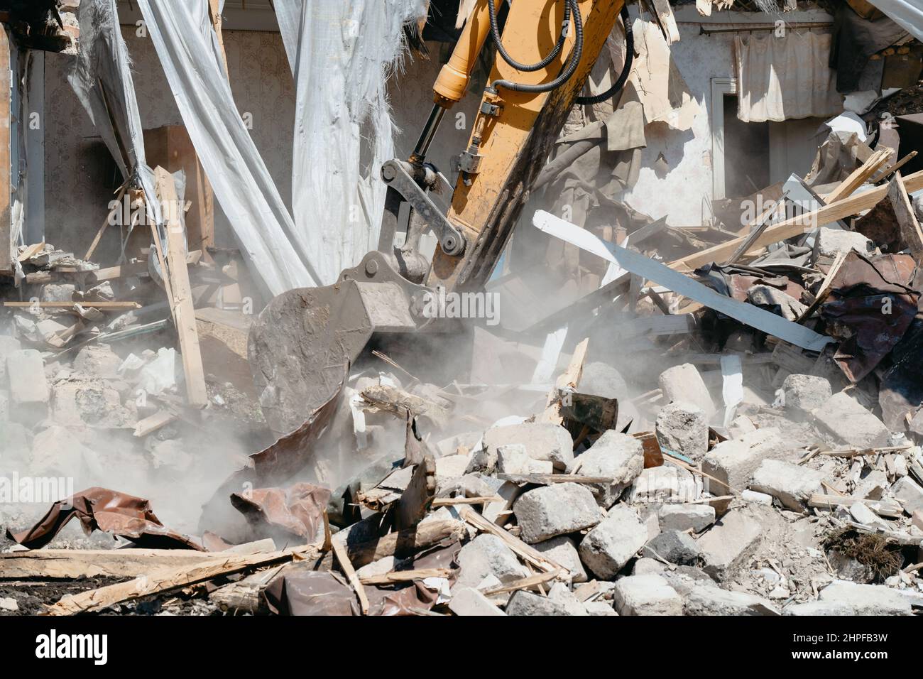 Close-up of excavator bucket raking in industrial debris. Demolishing of old dilapidated house for construction of modern housing. Stock Photo
