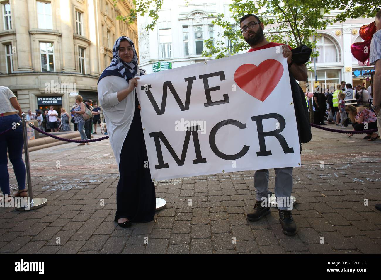 Young couple pose for the camera holding a We Love Manchester sign in the wake of the bombing in 2017. Stock Photo