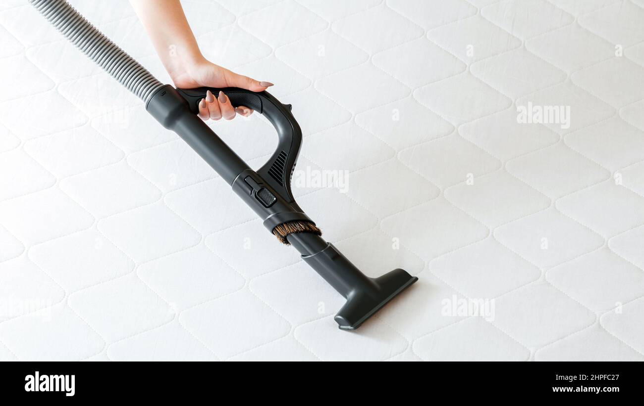 Vacuum cleaner machine in female hand do disinfection surfaces, cleanliness in hotel apartment. Woman do Professional cleaning mattress by vacuum Stock Photo