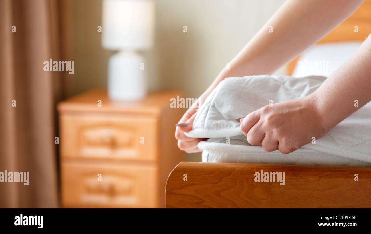 Woman puts on new mattress pad on mattress corner. Bed linen at home or