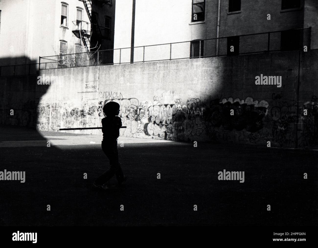 Silhouette of a young teenager playing stickball  and using a broomstick as a bat. In Park Slope, Brooklyn, New York City. Circa 1978 Stock Photo