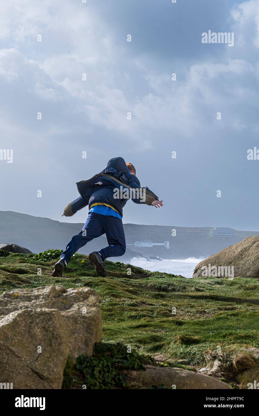 A young teenage boy having fun running into the storm force wind as Storm Eunice arrives in Cornwall in the UK. Stock Photo