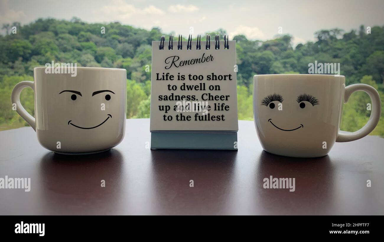 Motivational and inspirational quote on notepad. Life is too short to dwell on sadness. Cheer up and live life to the fullest. With coffee cups and Stock Photo