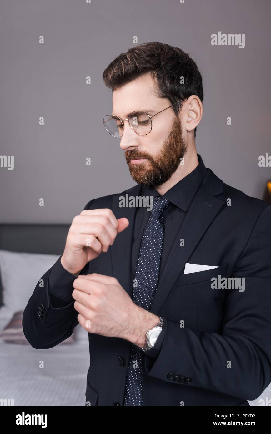 bearded man in eyeglasses adjusting sleeve of shirt in hotel room Stock Photo