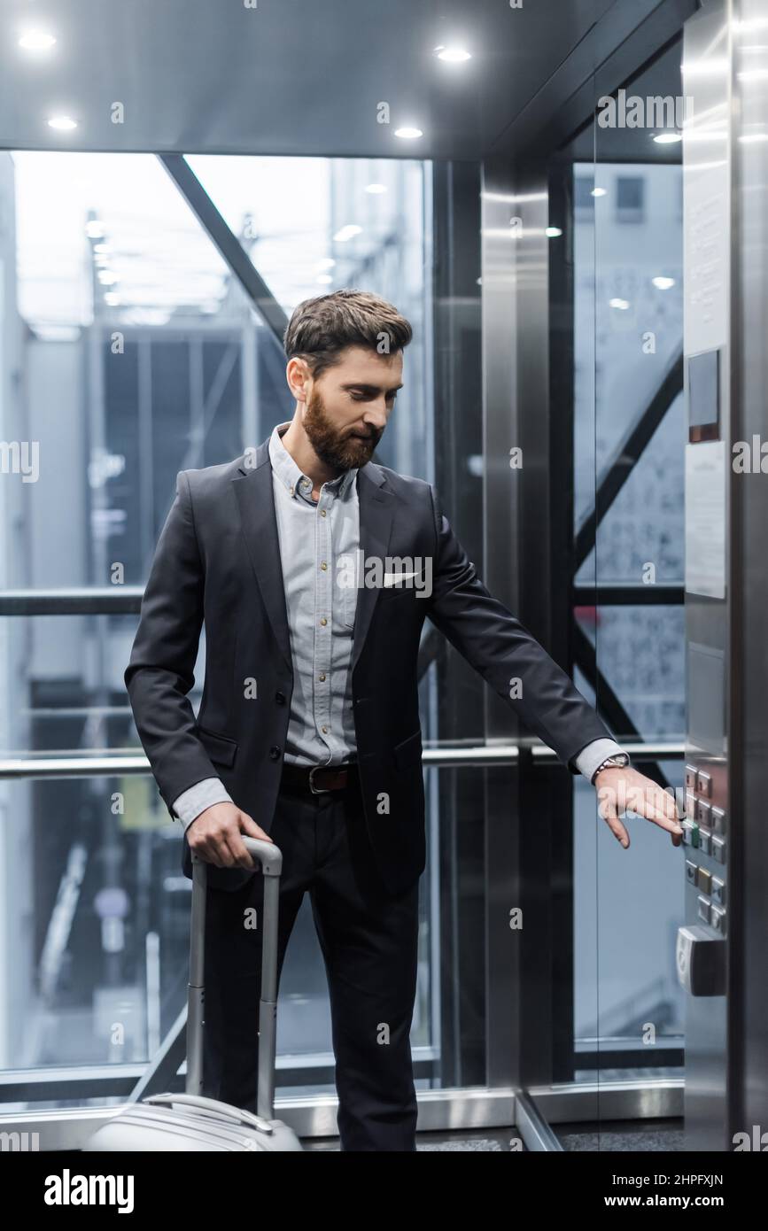 bearded man with baggage pressing button in modern elevator Stock Photo