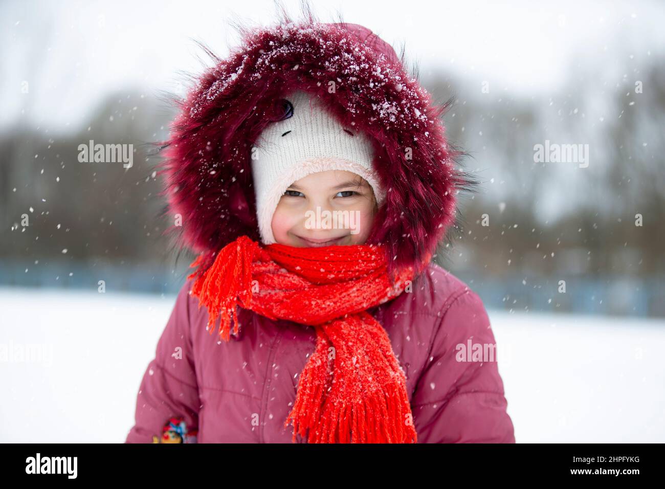 Child in winter. A little girl in a warm hat and hood looks at the camera and smiles. Stock Photo