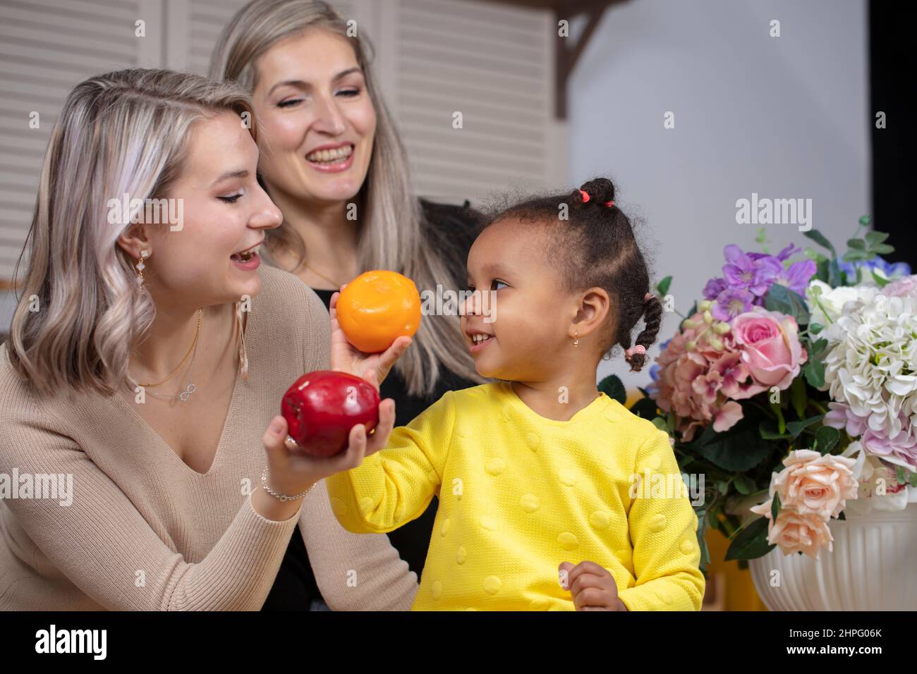 Family from different races. Mom grandmother light-skinned and a little African American girl play in the kitchen. Stock Photo